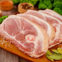 Sliced raw pork shoulder with spices on wooden board.