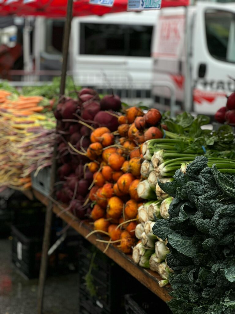 A vibrant display of fresh root vegetables and greens at an outdoor farmer's market, perfect for healthy living content.